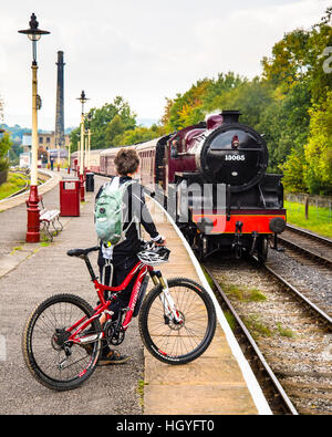 Woman with bicycle as steam train approaches at Rawtenstall on the East Lancashire Railway Stock Photo