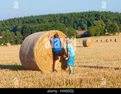 Two Boys Helping Each Other to Climb a Bale of Hay Stock Photo