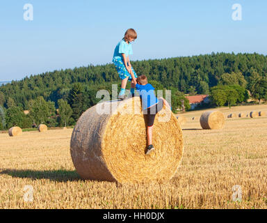 Two Boys Helping Each Other to Climb a Bale of Hay Stock Photo