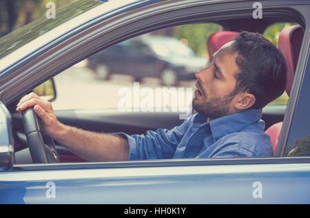 Side view sleepy tired fatigued exhausted man driving car in traffic after long hours. Transportation safety sleep deprivation Stock Photo