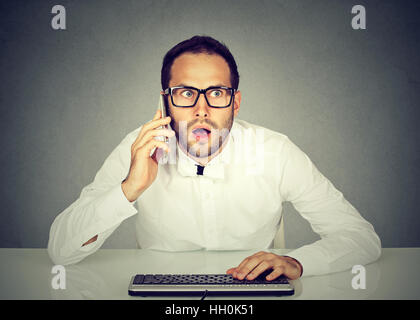 Shocked businessman talking on the phone while using computer Stock Photo