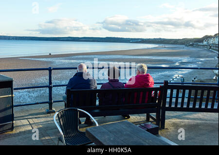 Three older people sitting on a bench overlooking the beach at Filey, North Yorkshire Stock Photo