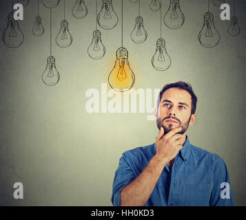 Portrait thinking handsome man looking up with idea light bulb above head isolated on gray wall background Stock Photo