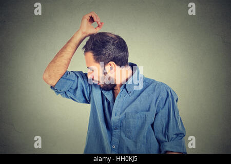 Closeup portrait of young man, smelling, sniffing his armpit, something stinks, very bad, foul odor isolated gray background Stock Photo