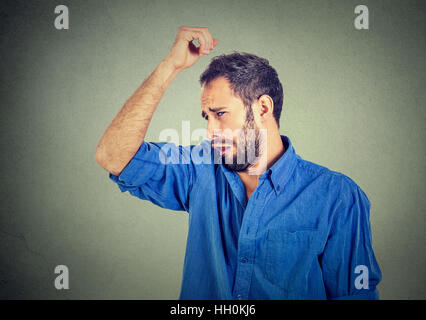 Closeup portrait of young man, smelling, sniffing his armpit, something stinks, very bad, foul odor situation, isolated on gray wall background. Negat Stock Photo