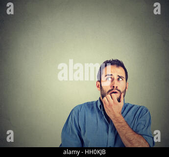 nervous stressed young man student biting fingernails looking up anxiously craving something isolated on gray wall background Stock Photo