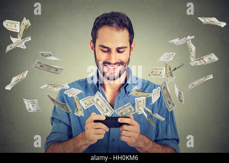 Technology online banking money transfer, e-commerce. Happy man using smartphone with dollar bills flying away from screen Stock Photo