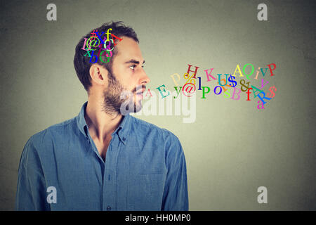 Side view portrait man talking with alphabet letters in his head and coming out of open mouth isolated on gray wall background. Human face expressions Stock Photo