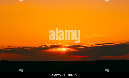 The Panoramic View Of Scenic Red And Orange Sunset On Dramatic Cloudy Sky Over Dark Field In Summer Spring Evening Dusk. Stock Photo