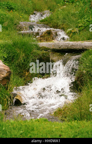 Close up view of stream flowing down the rocks surrounded by green grass Stock Photo
