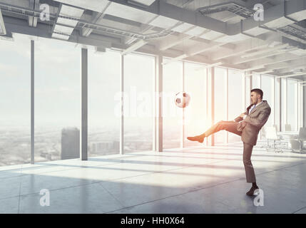 Young businessman in office interior playing football. Mixed media Stock Photo