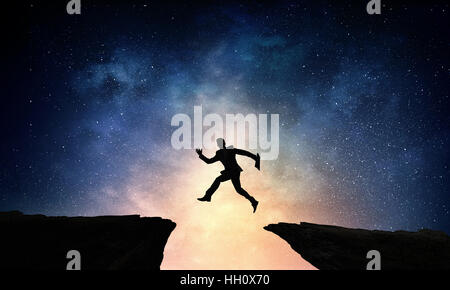 Silhouette of businessman jumping over hill gap against night sky background Stock Photo