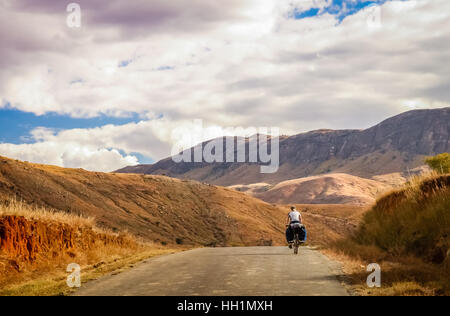 Woman cycling on the high plateau in central Madagascar Stock Photo