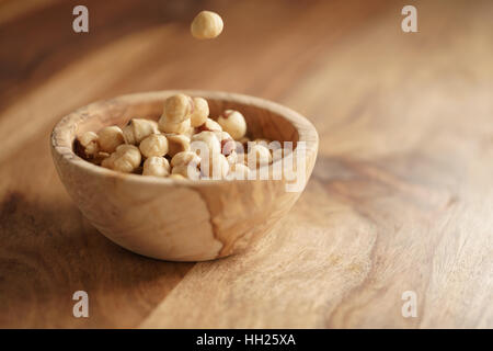roasted hazelnuts falling in wood bowl on wooden table Stock Photo