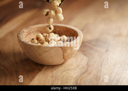 roasted hazelnuts falling in wood bowl on wooden table Stock Photo