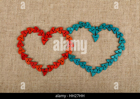 Two hearts together shaped of red and blue handmade wooden sewing buttons on linen canvas, elevated top view Stock Photo