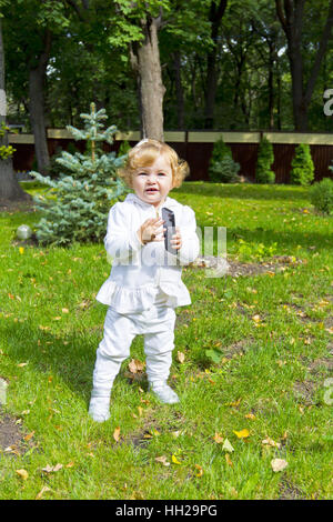 Cute baby girl with mobile phone on green grass Stock Photo