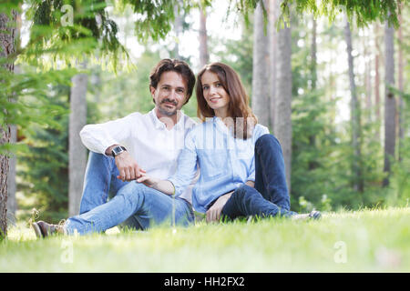 Happy couple sitting on grass in summer park Stock Photo