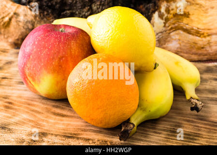 Fresh and ripe fruits on wooden cutting board. There is an apple, a blood orange, a lemon and two bananas on the board. Stock Photo