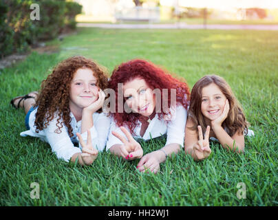 Red-haired mother and her two daughters lie on the grass in the summer Stock Photo