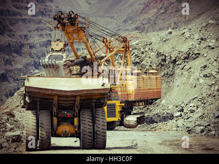 Heavy mining trucks and excavator working on the iron ore opencast mining facility Stock Photo