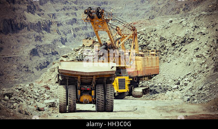 Heavy mining trucks and excavator working on the iron ore opencast mining site Stock Photo