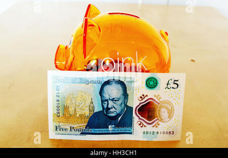 Back of the new polymer UK five pound note leaning against an orange piggy bank Stock Photo