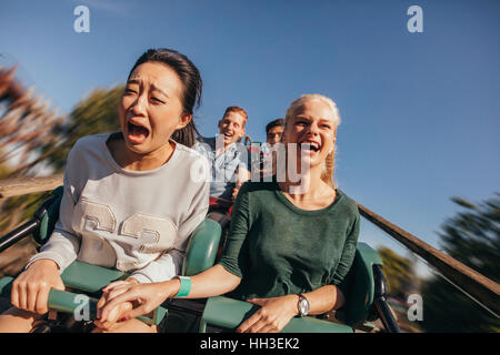 Shot of young friends cheering and riding roller coaster at amusement park. Young people having fun on rollercoaster. Stock Photo