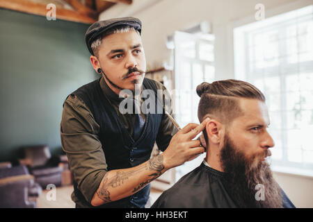 Hairdresser checking symmetry of haircut of his client at barbershop. Bearded man getting haircut by barber at barbershop Stock Photo