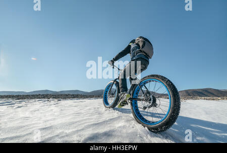 Fatbike also called fat bike or fat-tire bike - Cycling on large tire wheels. Cyclist goes to his bike on the frozen lake. Stock Photo