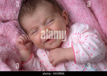A less than three weeks of age smiling baby girl, lying down on a pink blanket. Nouveau-né de moins de trois semaines souriant. Stock Photo
