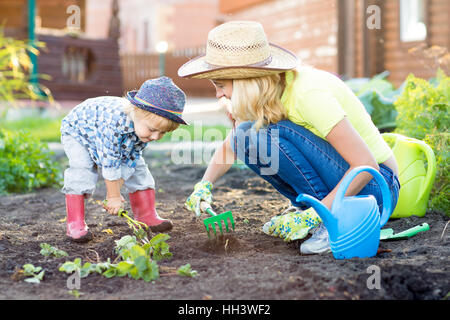 Kid and mother planting strawberry seedling into fertile soil outside in garden Stock Photo