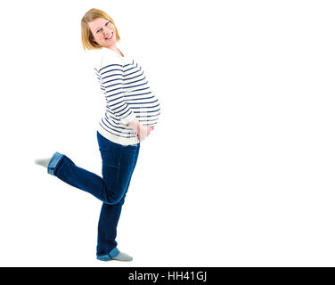 Pregnant blond woman in blue jeans and stripped sweater smiling and holding her belly with one leg lifted up. Isolated on white Place for your logo or Stock Photo