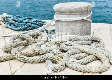 Old Stone Mooring on a stone paved pier with sea in the background Stock Photo