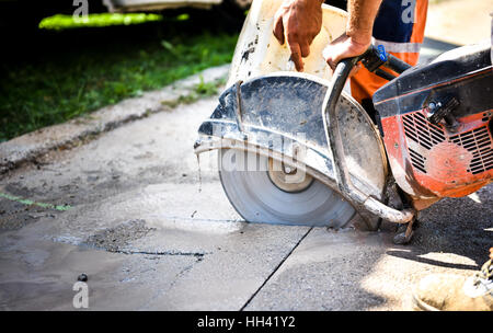 Construction worker cutting Asphalt paving stabs for sidewalk using a cut-off saw. Profile on the blade of an asphalt or concrete cutter with workers Stock Photo