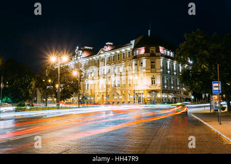 Vilnius, Lithuania. View Of Kempinski Hotel Cathedral Square In Bright Night Illumination On Universiteto Street . Moving Taxi Car With Red White Moti Stock Photo