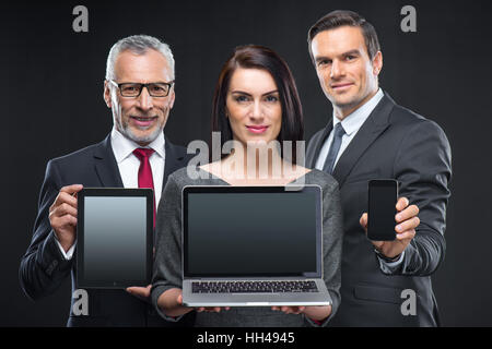 Portait of three businesspeople holding different devices on black Stock Photo