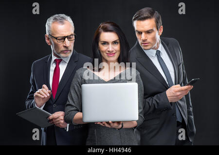 Portait of three businesspeople holding different devices on black Stock Photo
