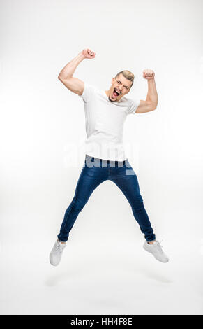Full length portrait of exited young man jumping on white Stock Photo