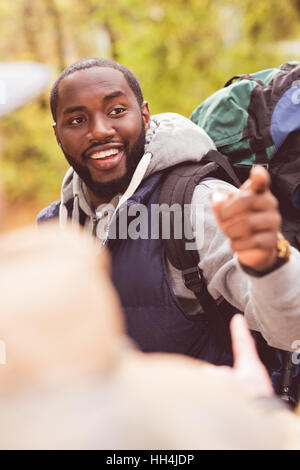 Young smiling man backpacker pointing with finger and talking with blurred male friend on foreground Stock Photo