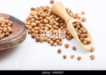 Aromatic color coriander seeds ingredient on white table with wooden rustic scoop and red fabric bag in background Stock Photo