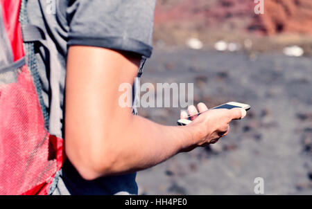 closeup of a young caucasian man carrying a backpack using a smartphone outdoors, in the mountain Stock Photo