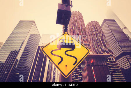 Color toned slippery when wet road sign with curvy tracks, Chicago skyscrapers in distance, conceptual picture. Stock Photo