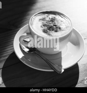 Cappuccino. Cup of coffee with milk foam and cinnamon powder stands on wooden table, square black and white photo Stock Photo