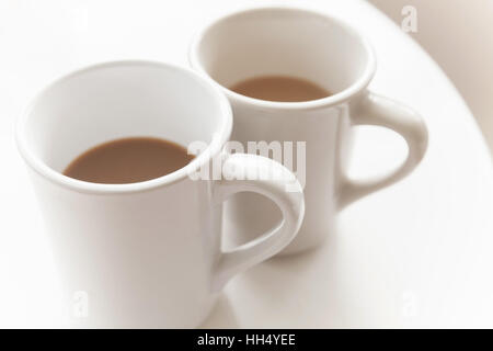 Two big cups full of coffee with milk stand on white table, closeup photo with selective focus