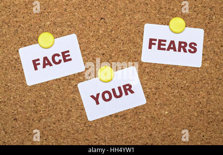 Text Face Your Fears on white stickers pinned on cork board Stock Photo