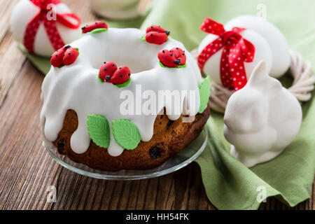 Easter sweet ring cake with glace icing decoration and white easter eggs with red bow on rustic wooden table Stock Photo