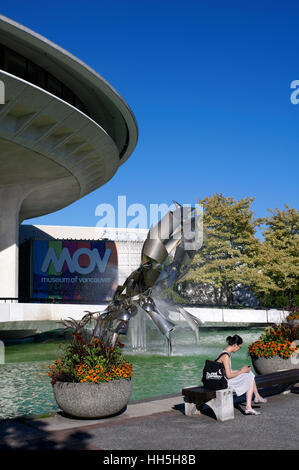 Young Asian woman using her cell phone with H.R. MacMillan Space Centre and Museum of Vancouver  in background, Vancouver, British Columbia, Canada Stock Photo