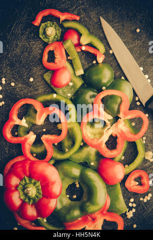 Cutting board and knife with fresh organic red and green bell peppers sliced and chopped for meal preparation. Stock Photo