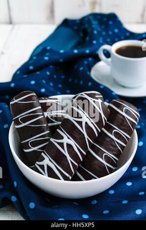 Fragrant cookies of choux pastry in dark chocolate covered with white decoration  and cup of coffee on blue napkin Stock Photo